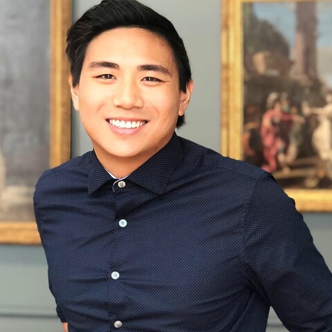 Short haired man with navy button down, smiling in front of a classical painting