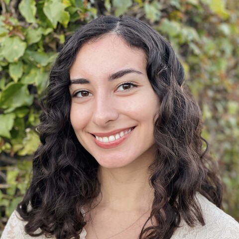 Woman with curly shoulder length hair and white lace shirt in front of ivy wall