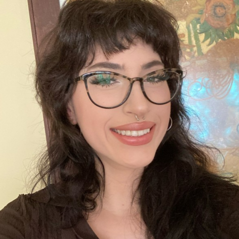 Woman with shag haircut, cat-eye glasses, and black shirt, standing in front of Van Gogh sunflowers