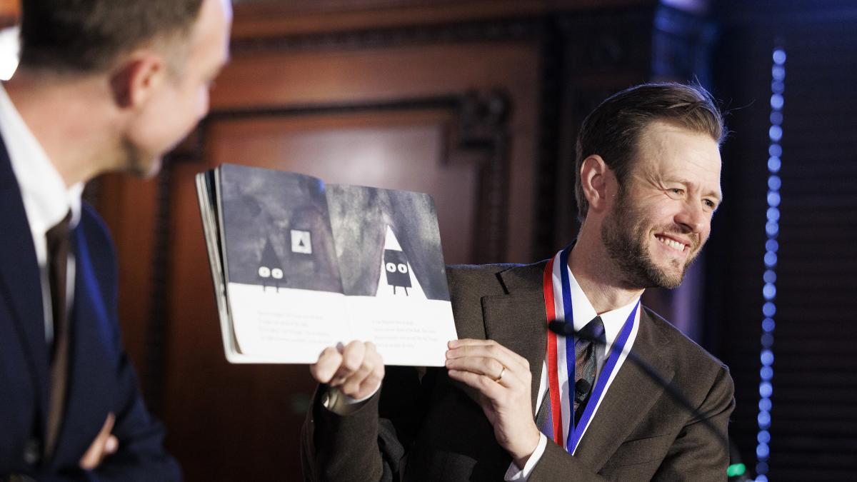 Mac Barnett on stage holding one of his picture books