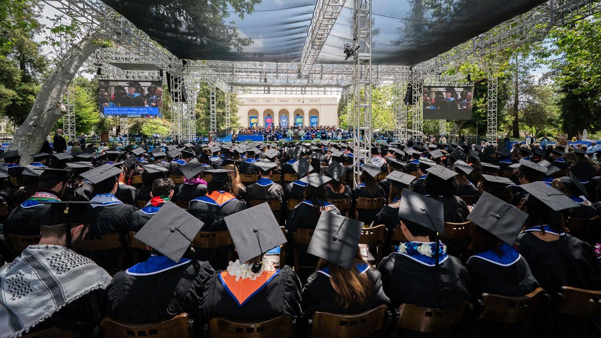 Class of 2025 wearing caps and gowns and seen from behind while sitting at commencement.