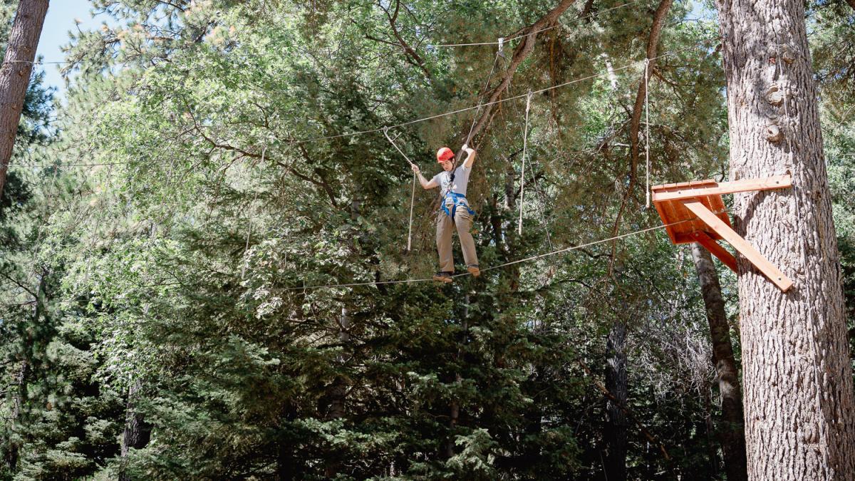 Student walking across a tightrope stretched across trees in the mountains.