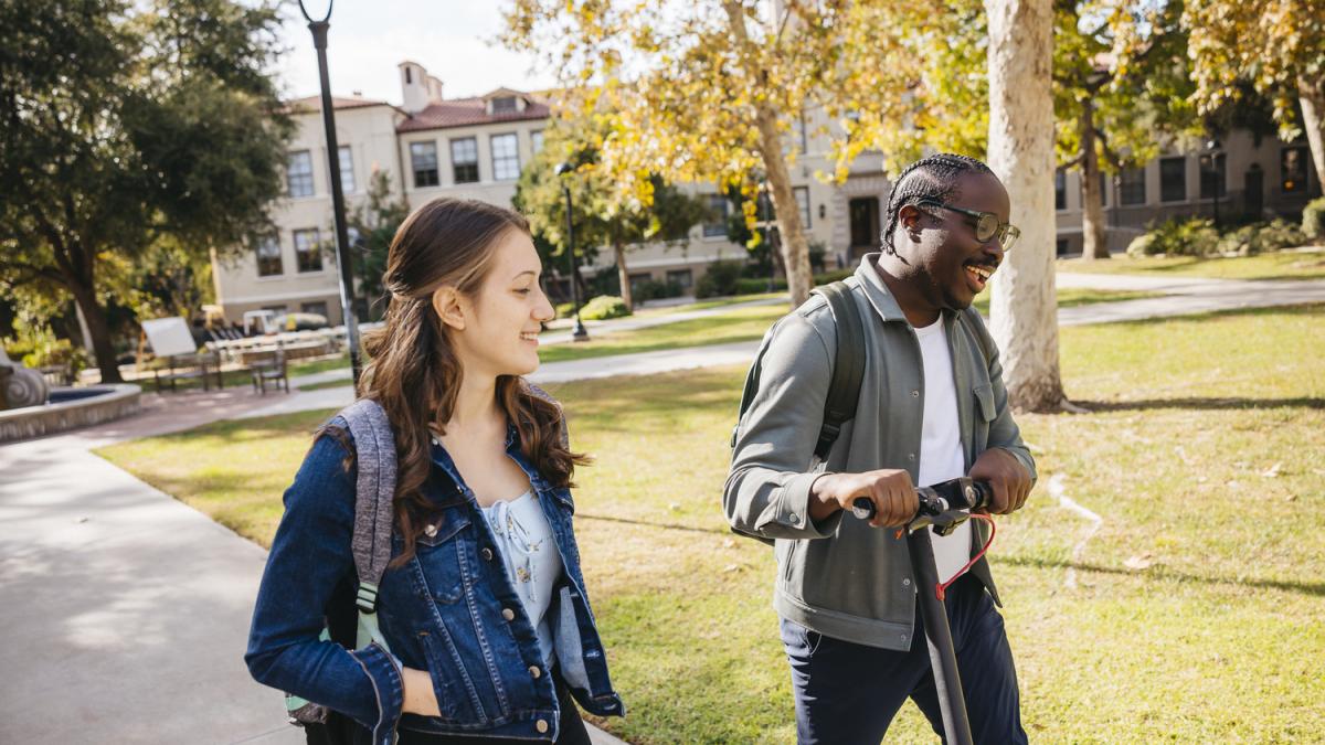 Two students walking and talking in front of academic building.
