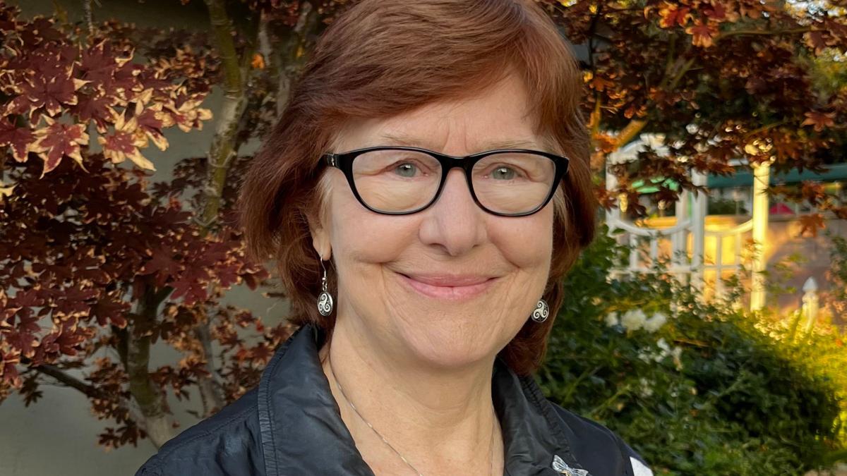 A woman in glasses stands and smiles