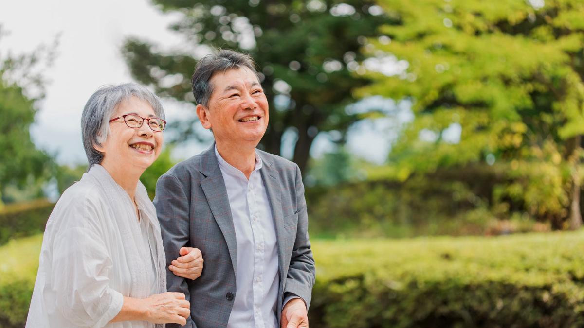 Older couple walking outdoors with trees and grass in background