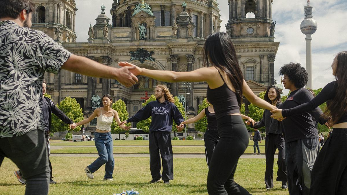Student hold hands and dance in a circle outdoors in Berlin.