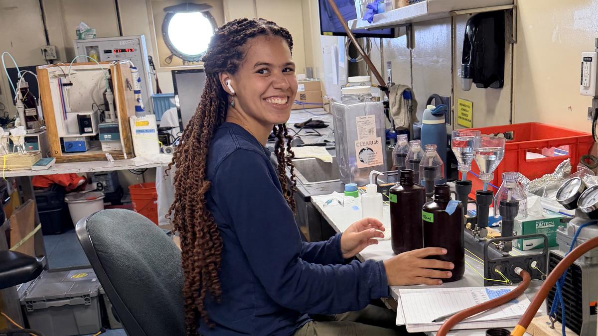 Elle Hawthorne seated at a table filled with scientific instruments on board a research ship.