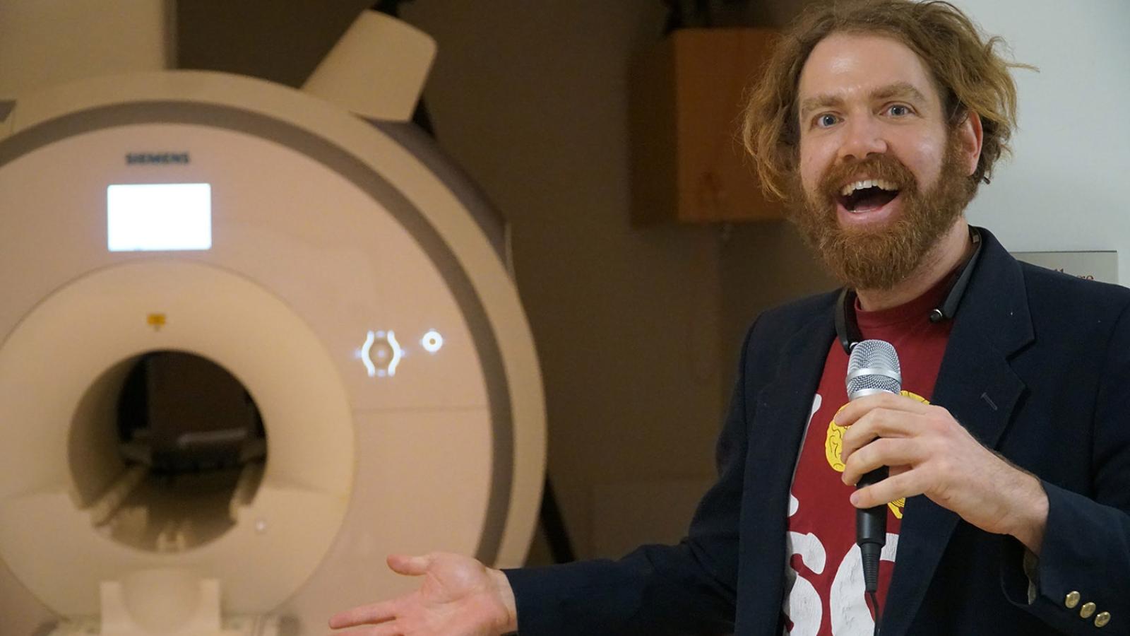 Professor Ori Amir holds microphone while standing by machine.