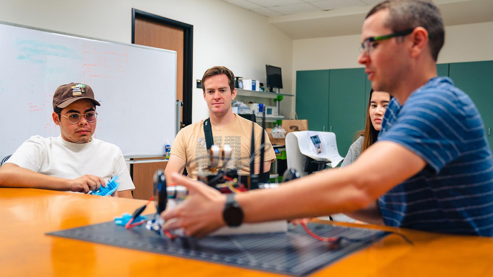 Computer science professor Anthony Clark and three students work on robot.