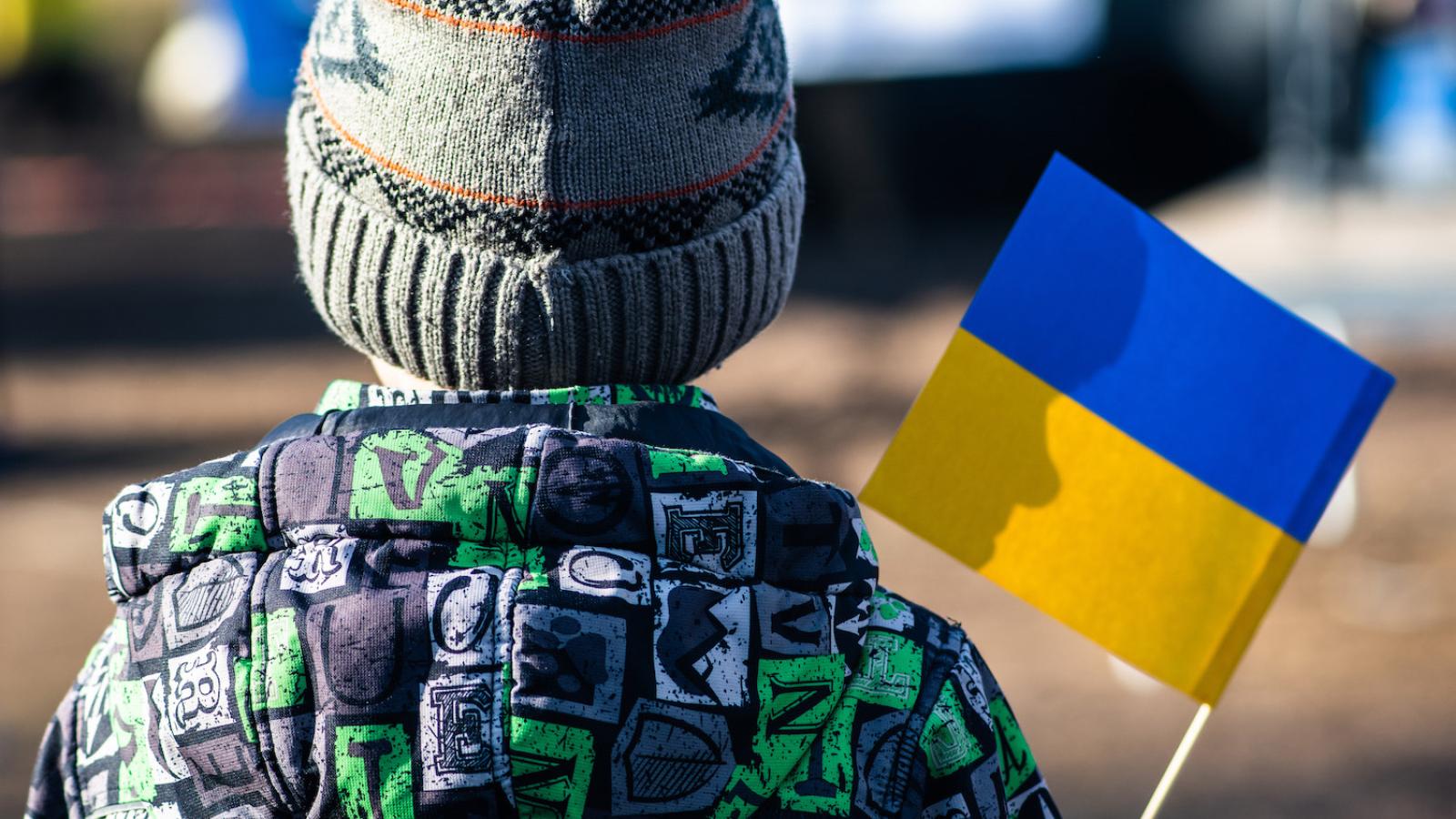 Back of refugee child waving a Ukrainian flag