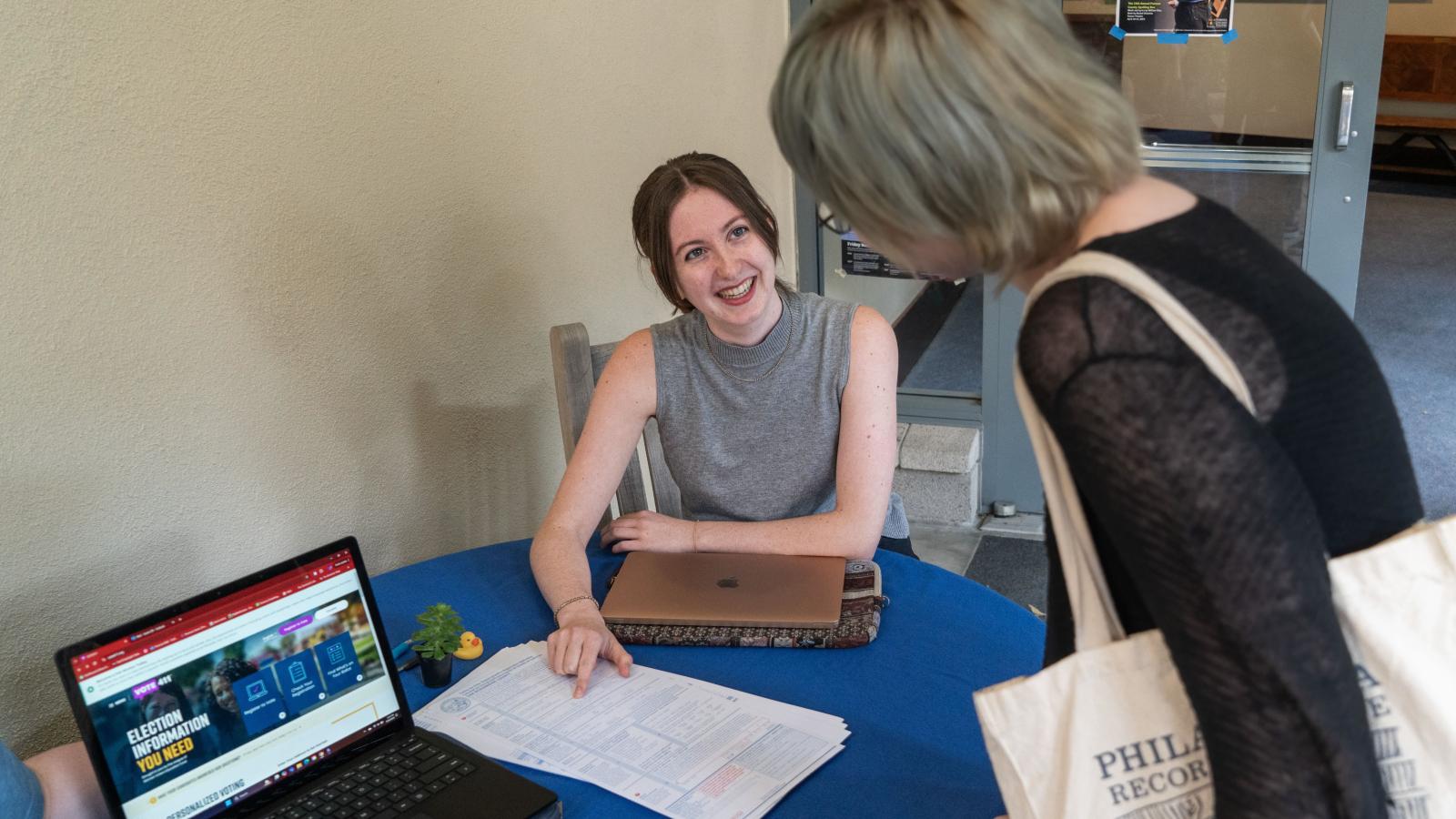 A student sits at a table and talks to a woman