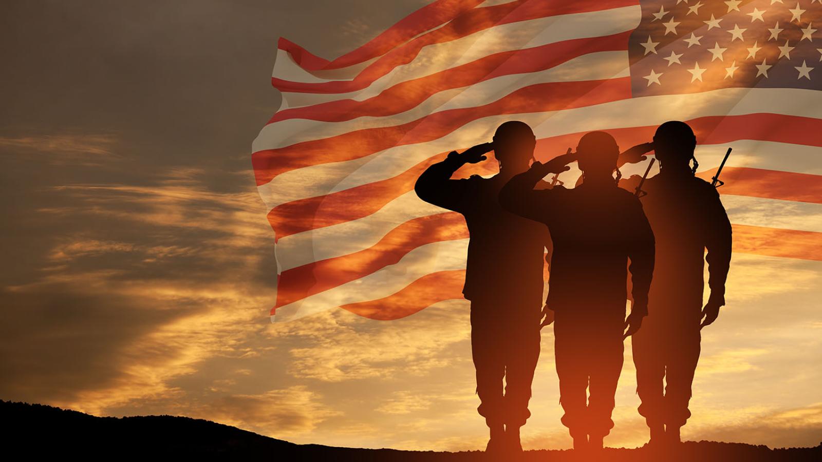 Photo at sunset with the American flag and three military service members saluting