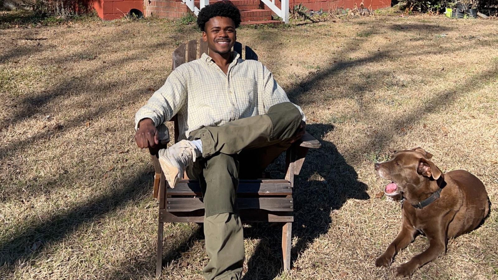 Ivan Soloman sits on a chair outside with his dog on the ground next to him.