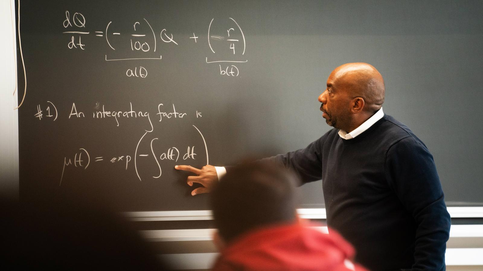 Edray Goins points to a chalkboard in a classroom.