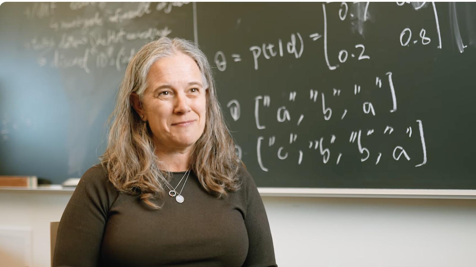 Professor sits in front of a chalkboard 