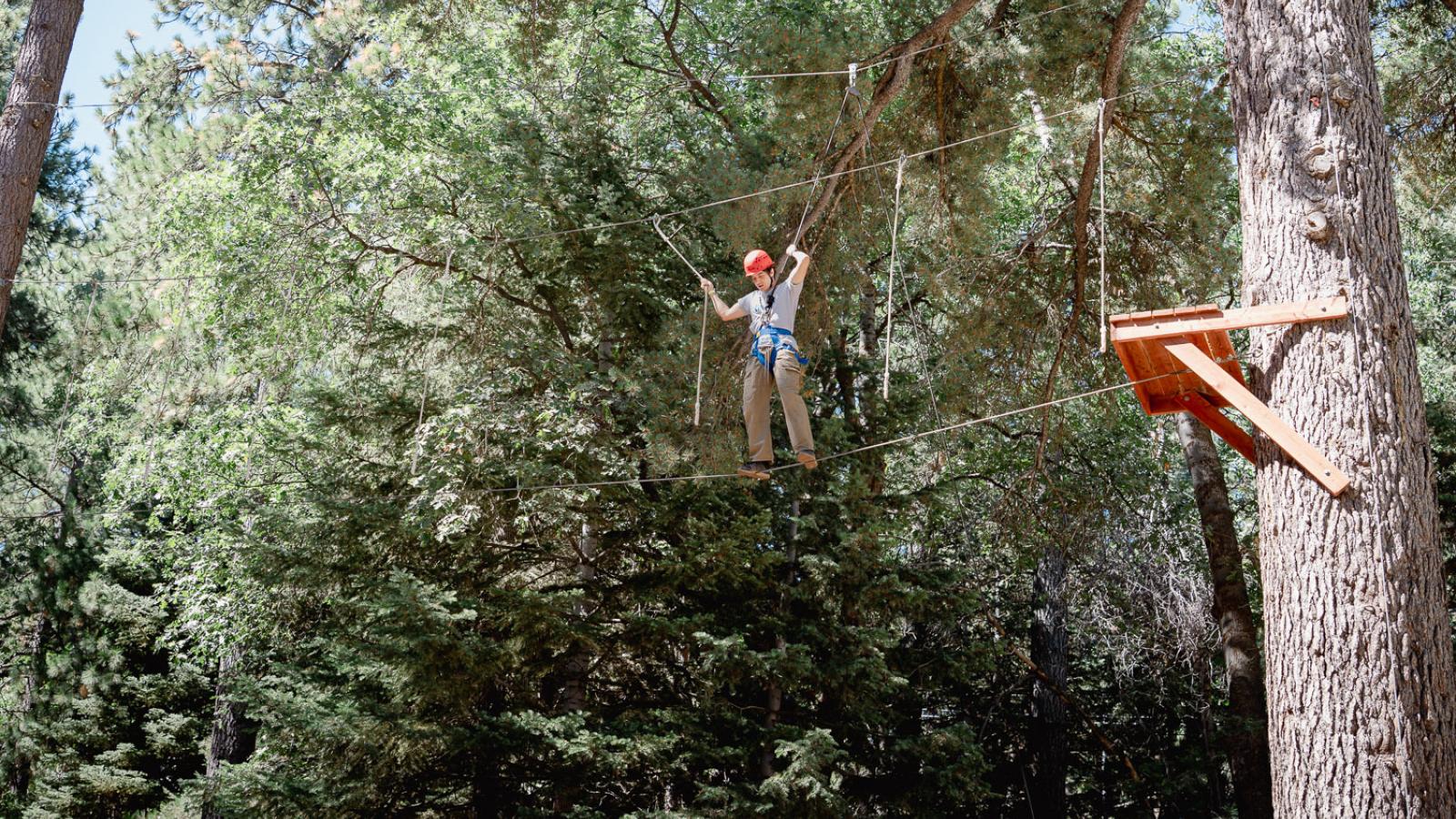 Student walking across a tightrope stretched across trees in the mountains.