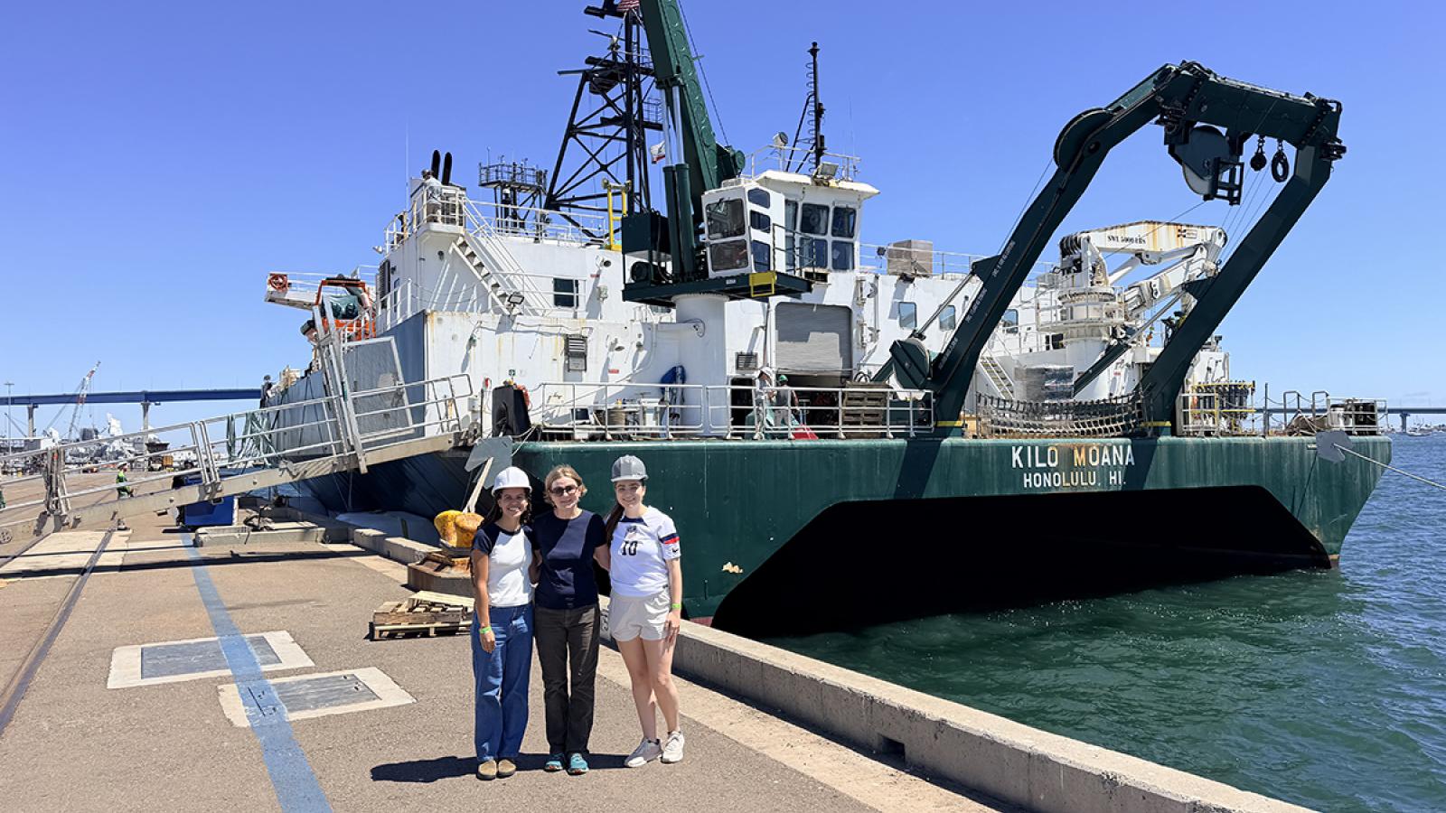 Three members of the Pomona research team stands in front of the research ship in San Diego harbor.