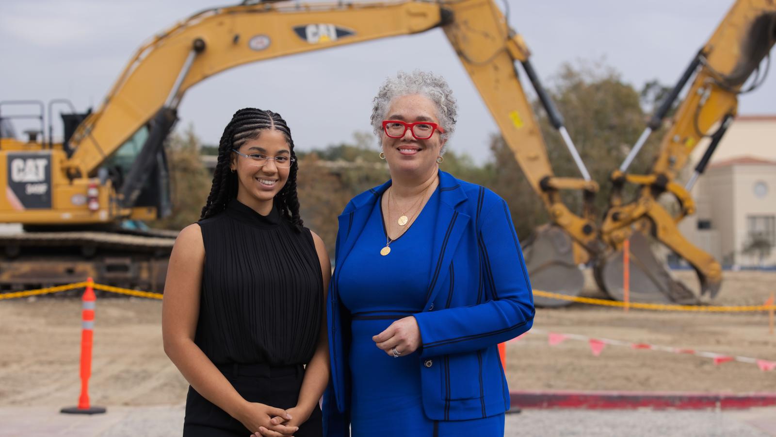 Two women in front of an excavator
