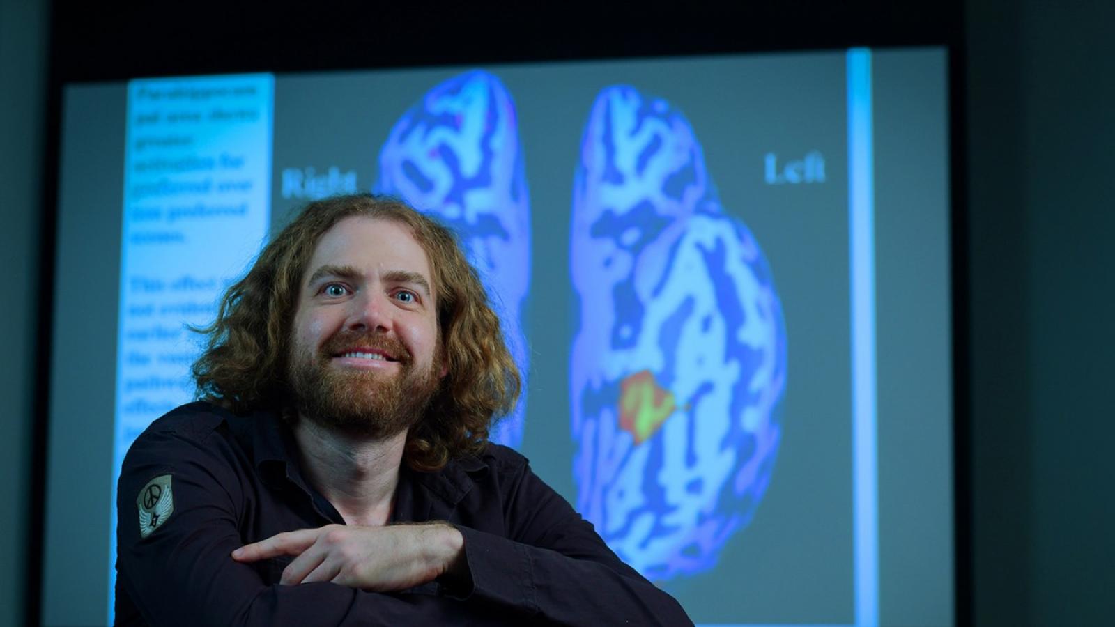 Professor Ori Amir with screen showing hemispheres of brain behind him