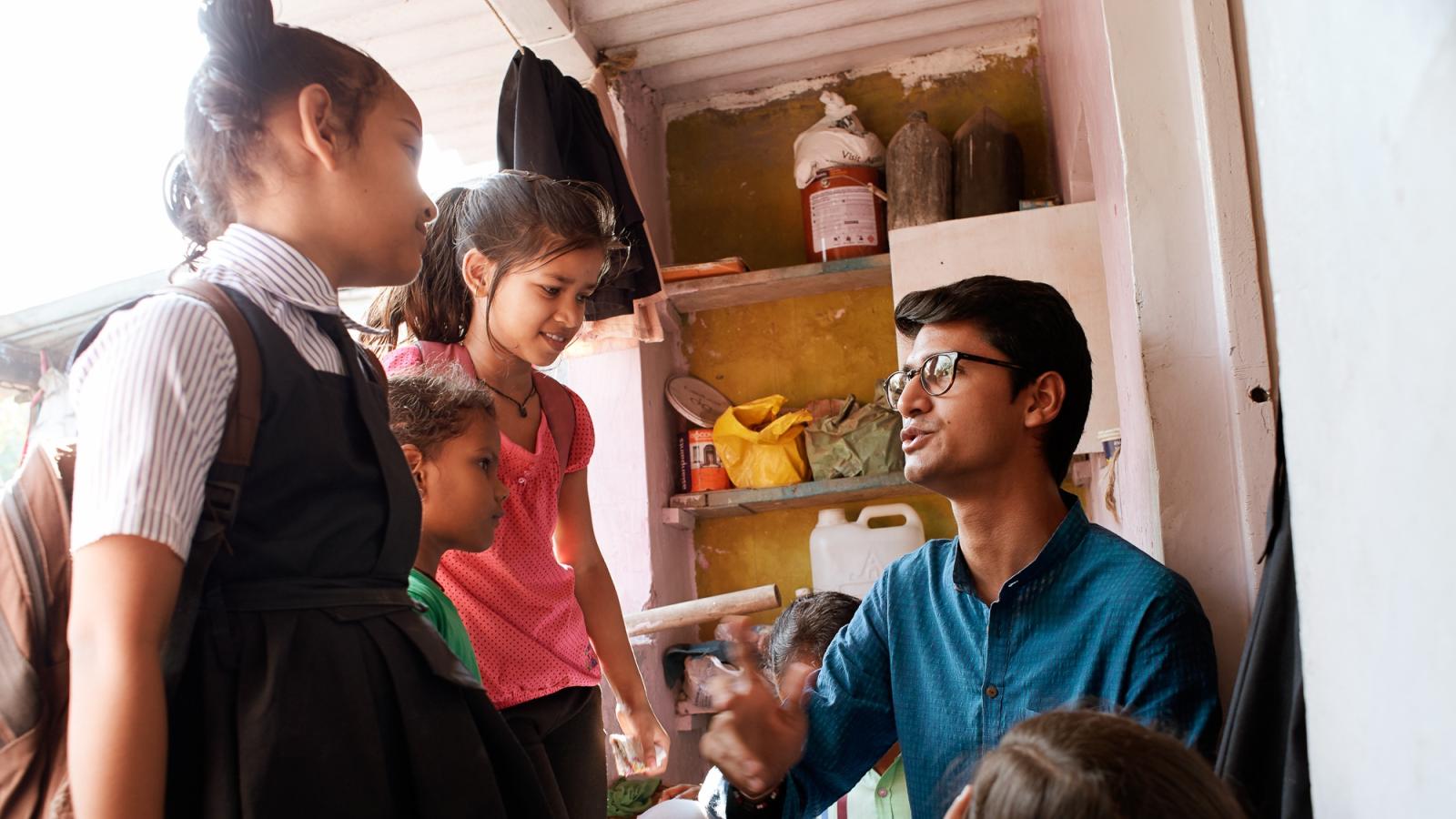 Aaran Patel sits in classroom with three children to the left of him.