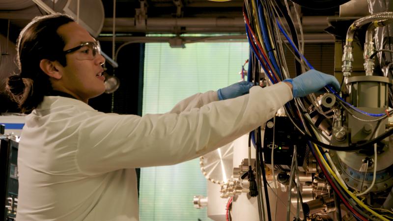 Scott Tan in profile in lab gear is working with computer wires.