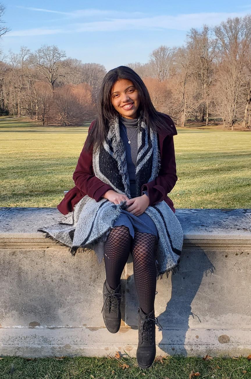 Anaelle Roc sits on a small wall in a green park.