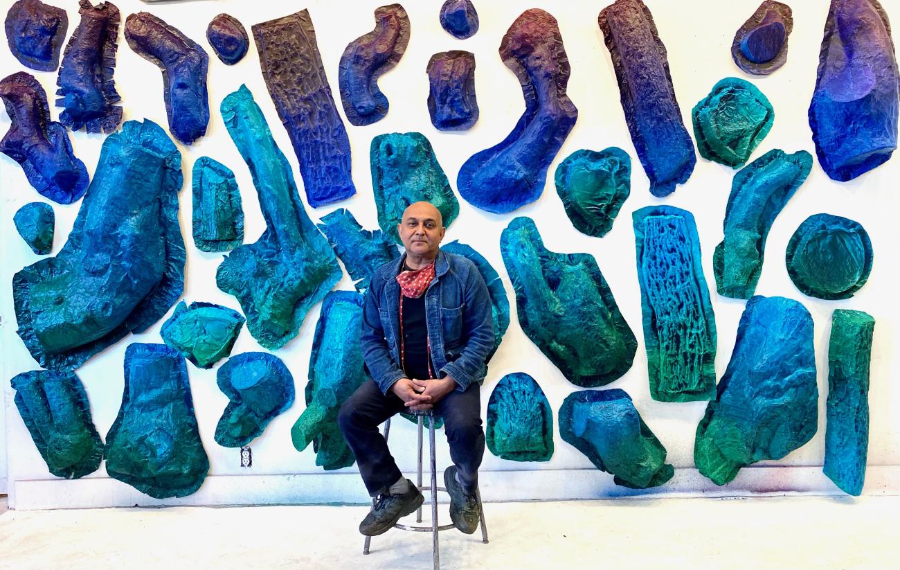 Artist Sandeep Mukherjee seated in front of blue-hued components of his YouTube Theater installation.