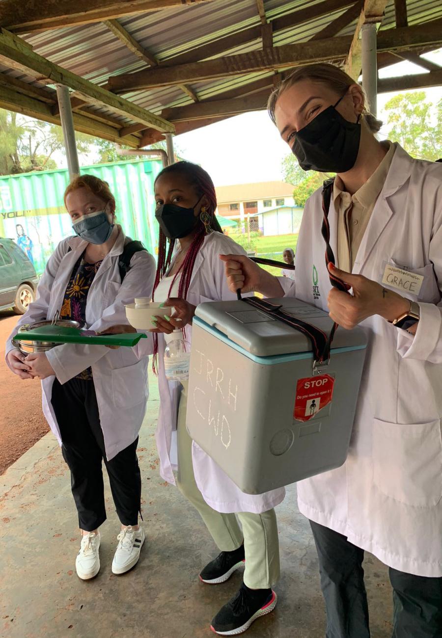 Three SIT students wearing white lab coats, standing outdoors in Kenya