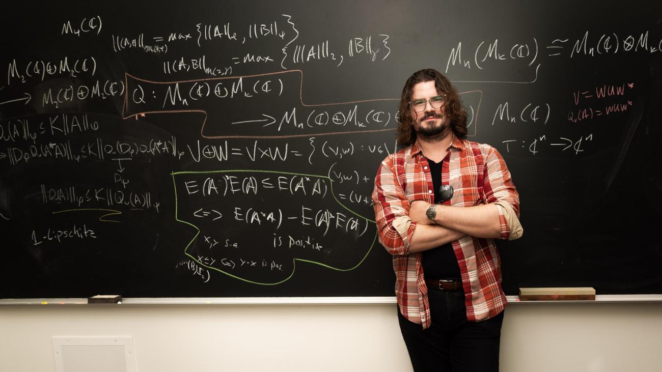 Konrad Aguilar standing in front of blackboard that is covered with mathematical formulas