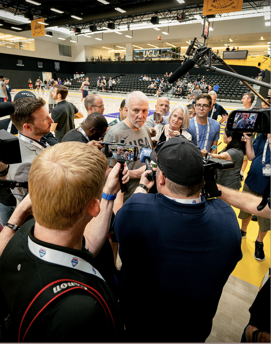 Popovich surrounded by media in gym. 