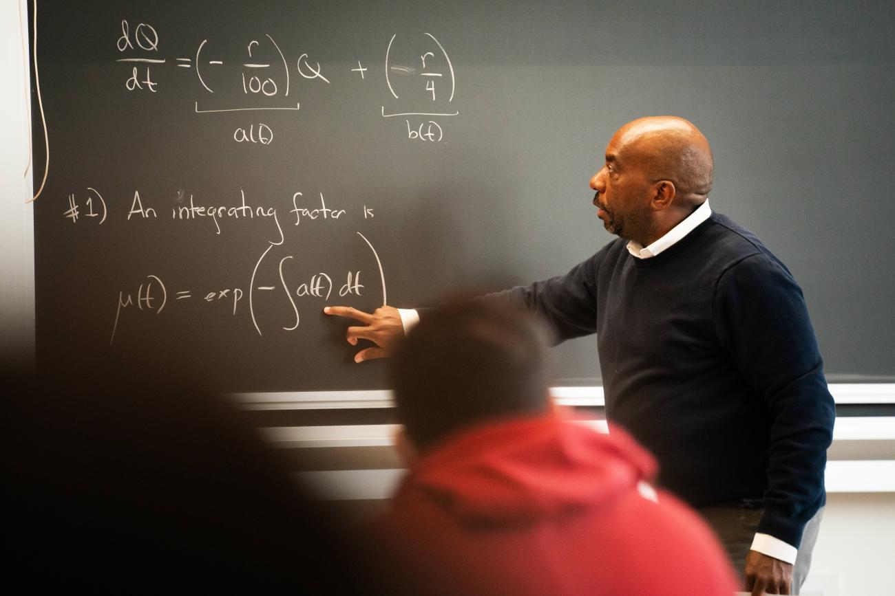 Edray Goins points to a chalkboard in a classroom.