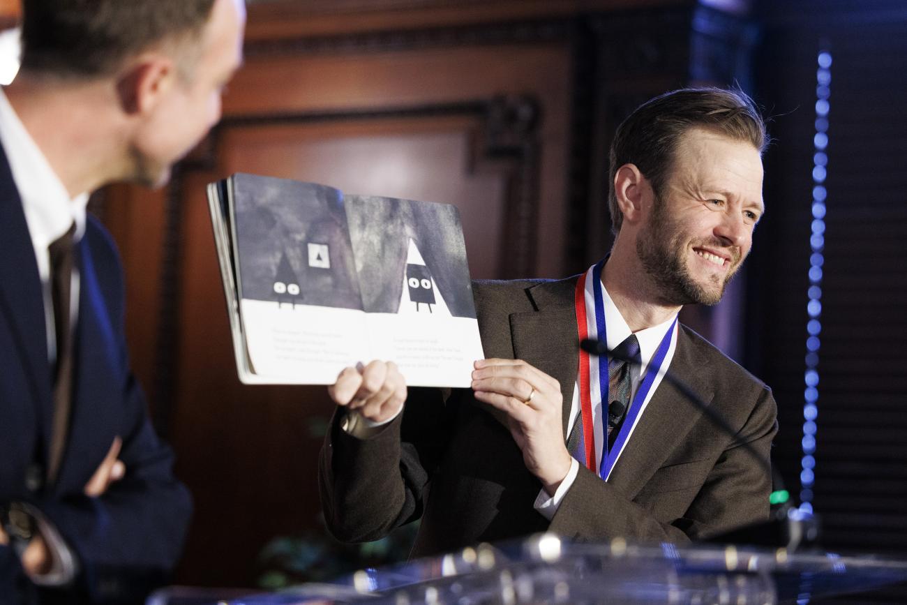 Mac Barnett on stage holding one of his picture books