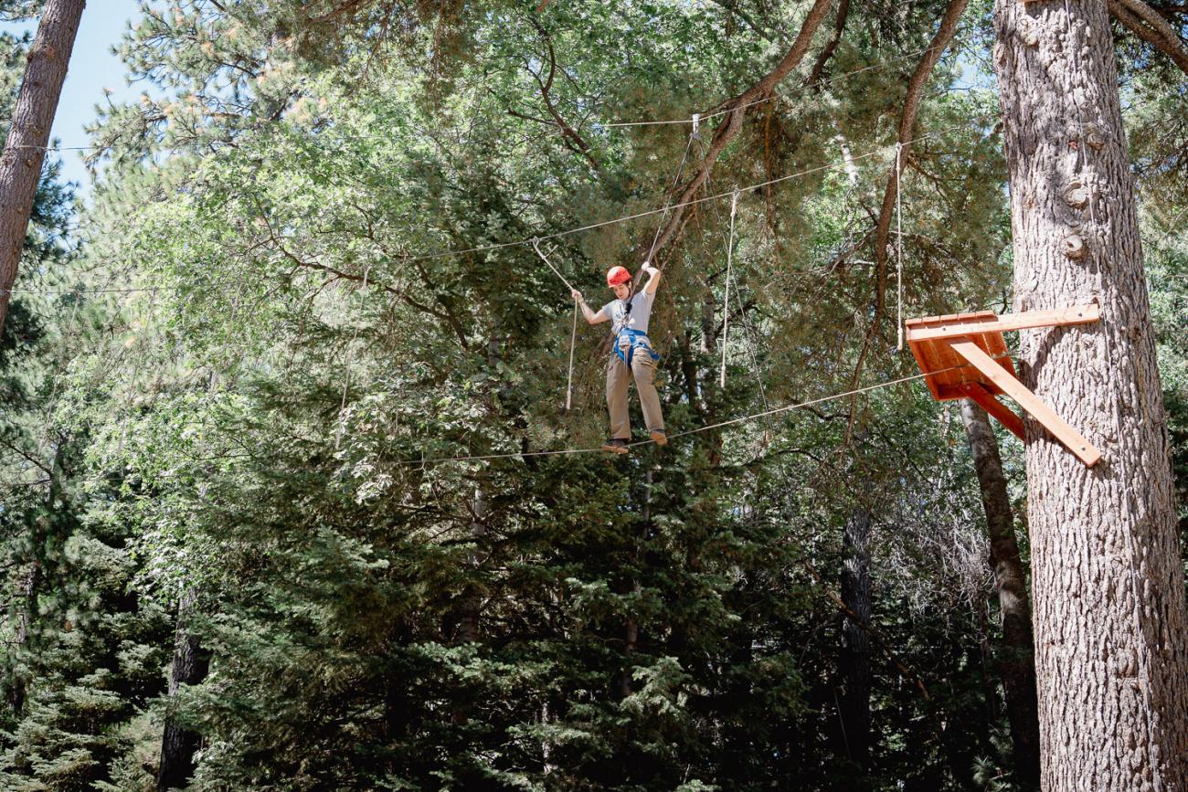 Student walking across a tightrope stretched across trees in the mountains.