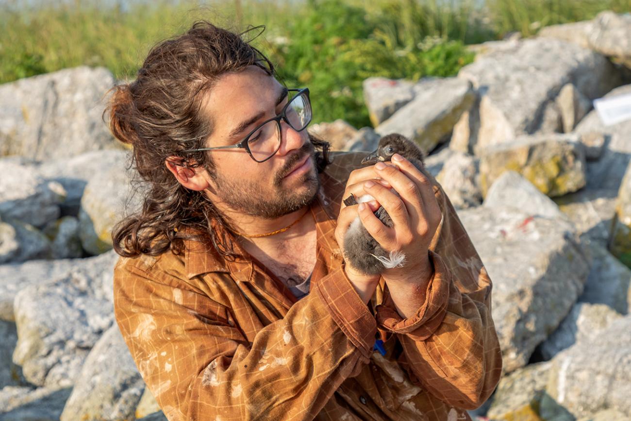 Jacob Ligorria holding seabird chick with rocks in background