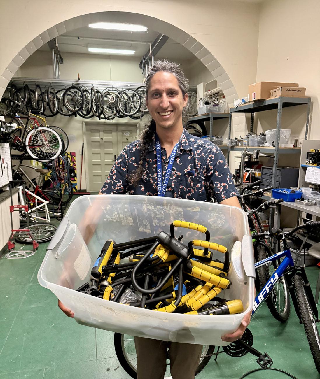 Nikhail Schneider holds basket of bicycle locks in green bike room.