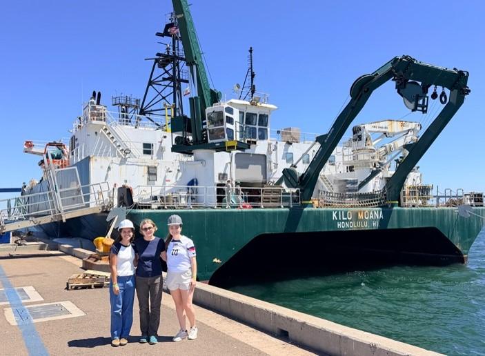 Masha prokopenko, Elle Hawthorne and Charlotte Renner pose next to the research vessel