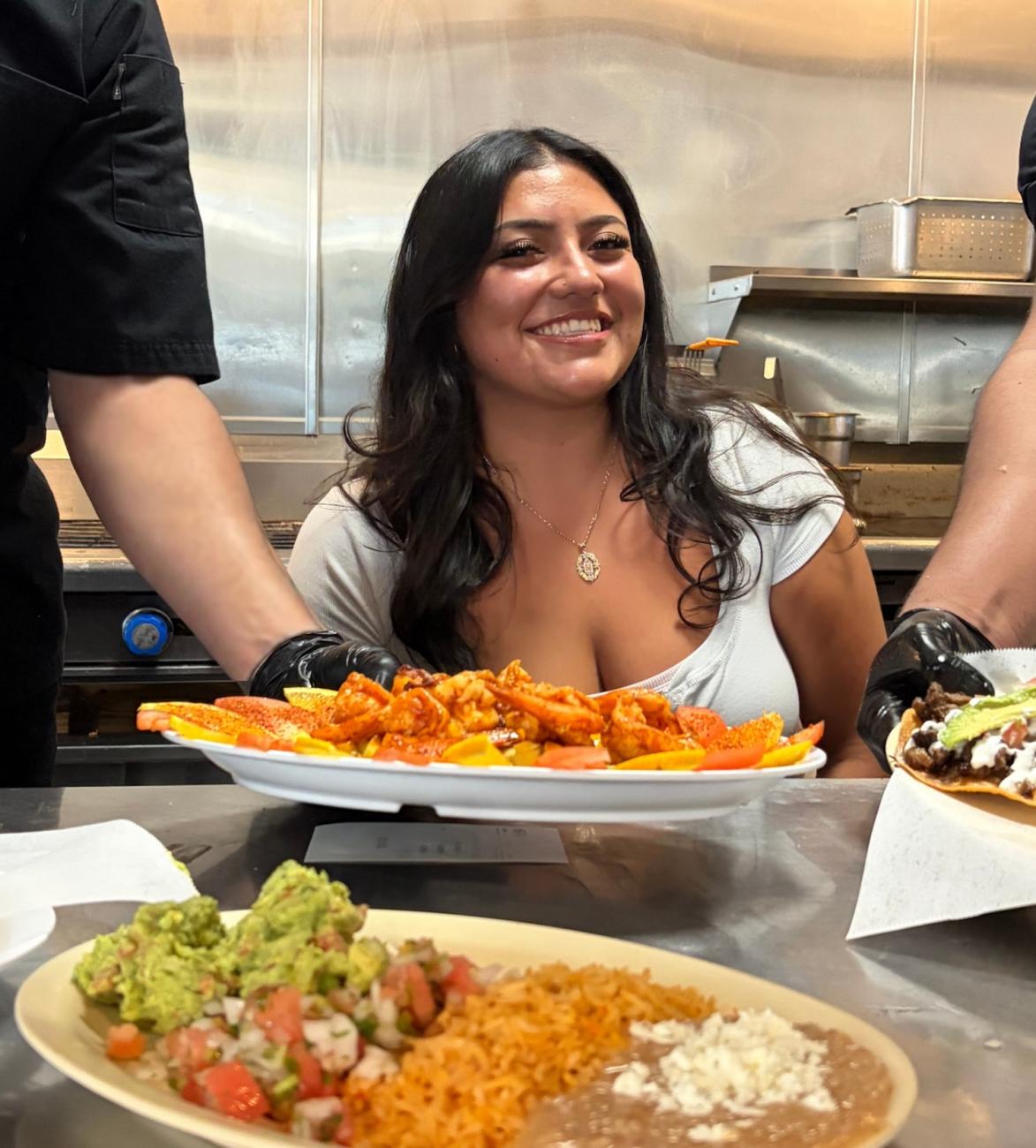 Woman being served plates of Mexican food in a restaurant kitchen
