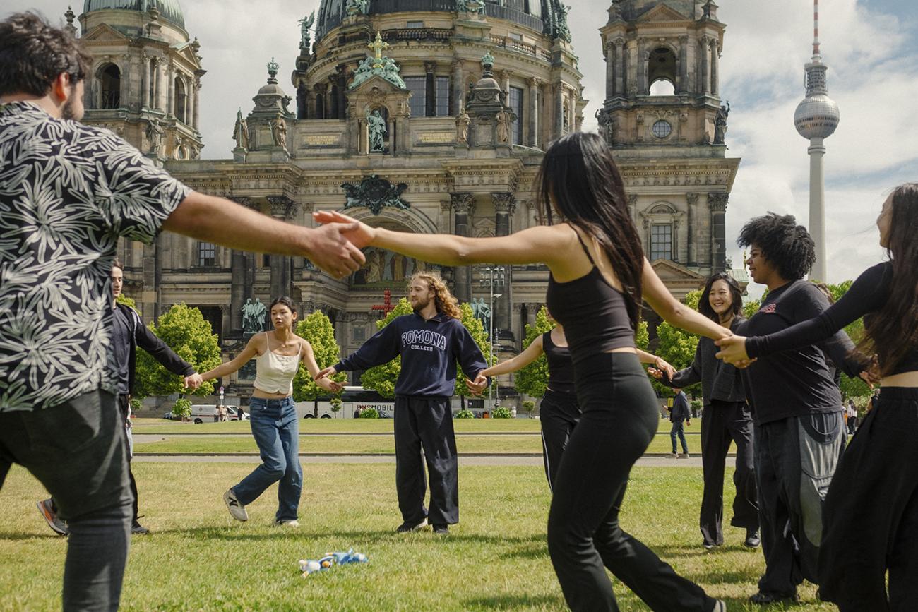 Student hold hands and dance in a circle outdoors in Berlin.