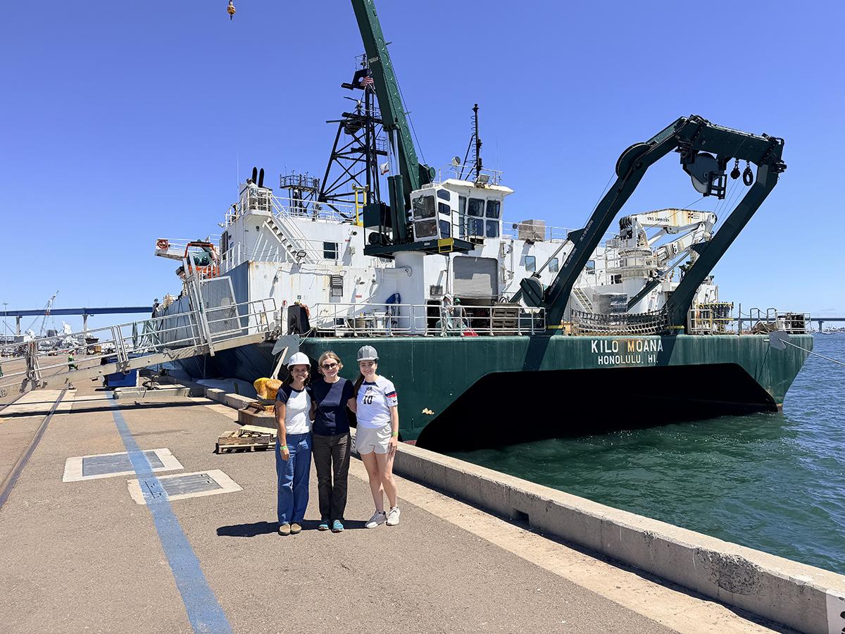 Three members of the Pomona research team stands in front of the research ship in San Diego harbor.