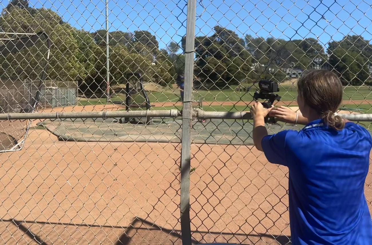 A woman points a camera toward a baseball field