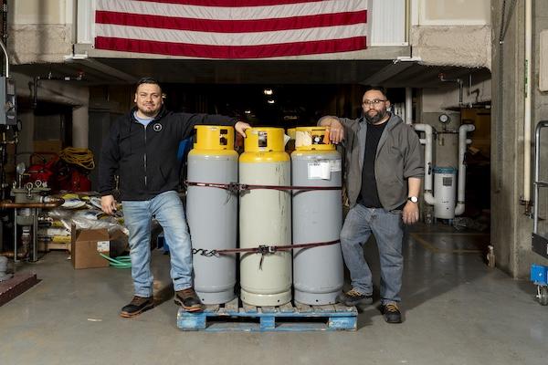 Two men stand with tanks of refrigerants to be destroyed.