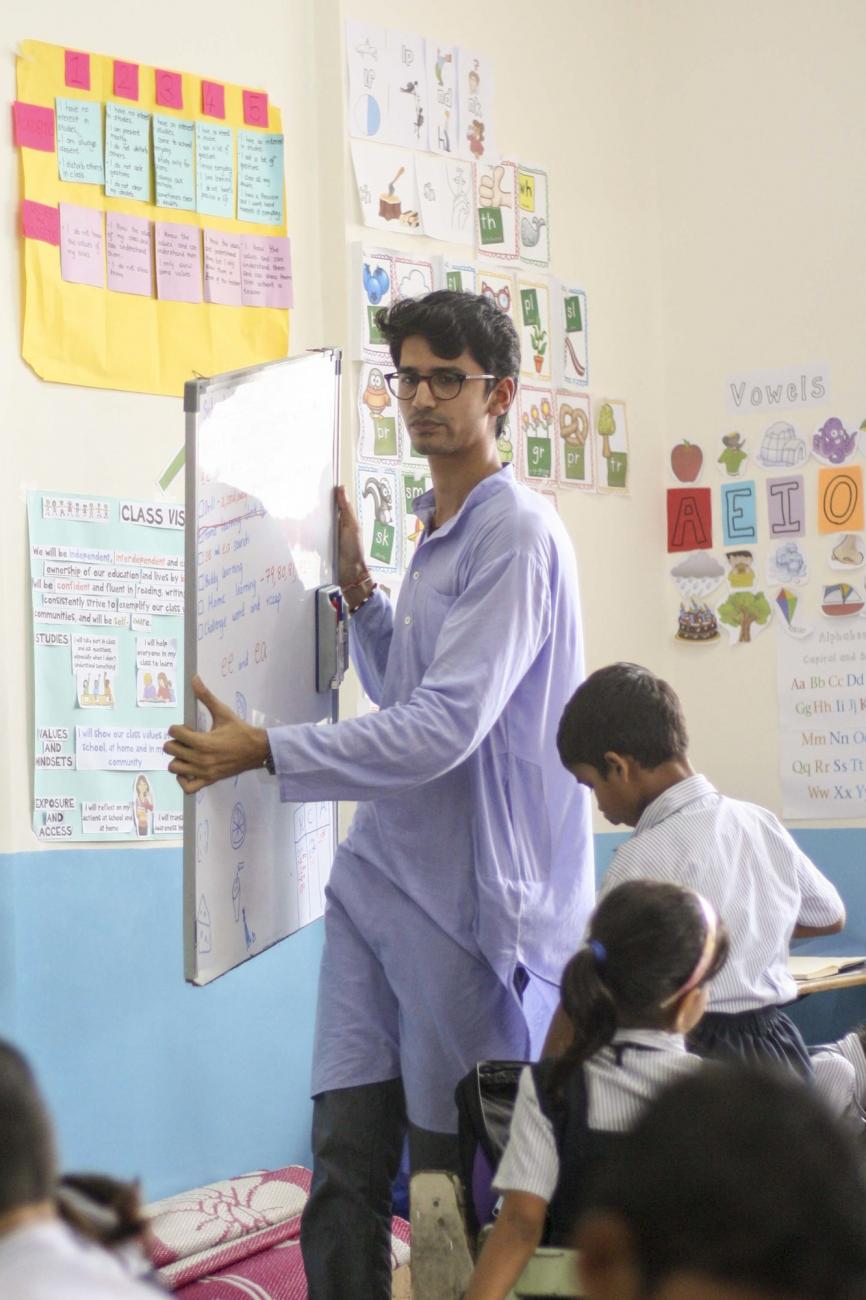 Aaran Patel in front of classroom holding board in his hands.