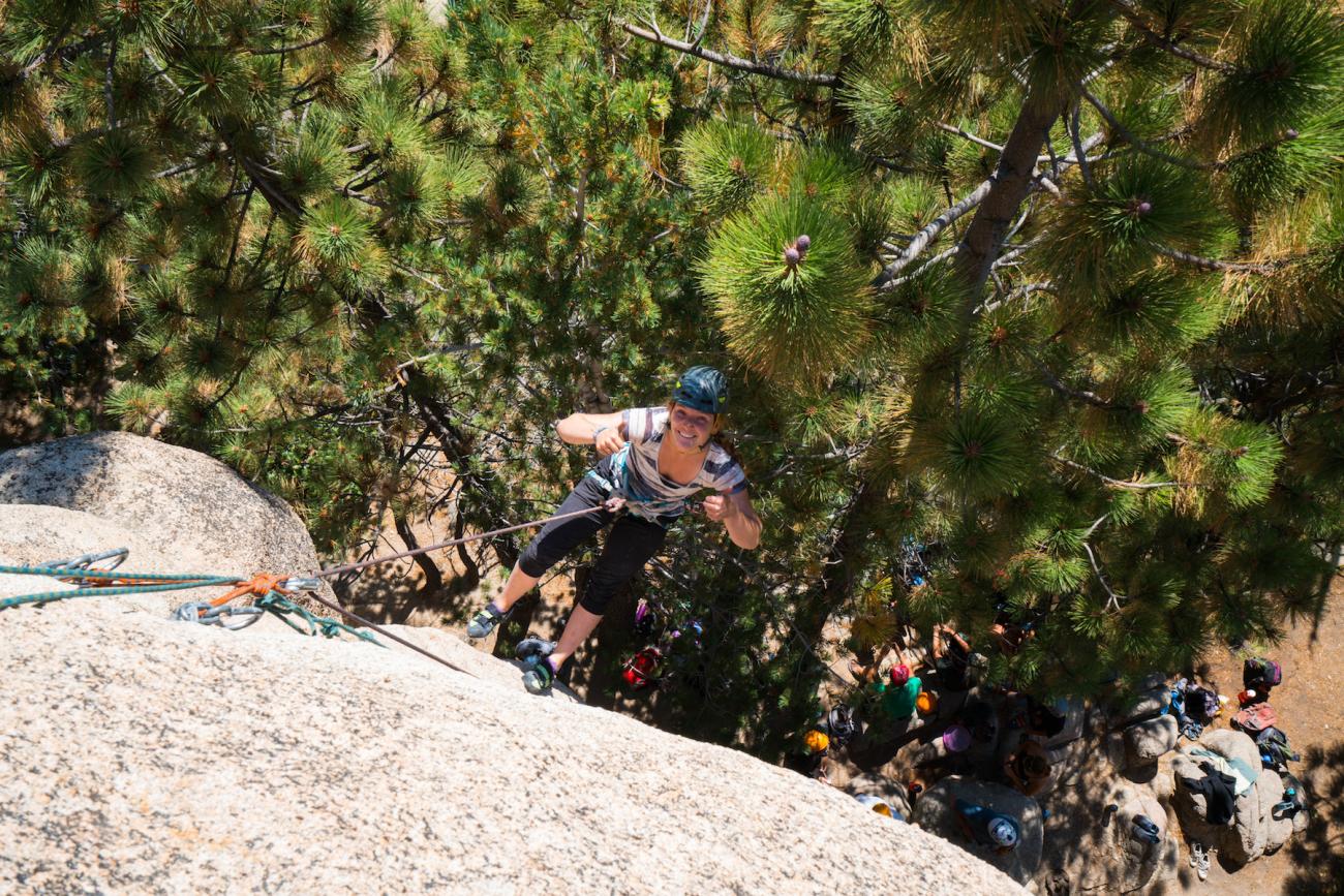 Student gives thumbs up as she climbs up the rock face.