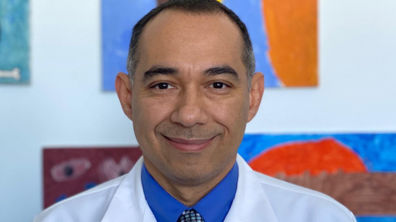 Dr. Edgar Chavez '98 in medical white coat in front of colorful background