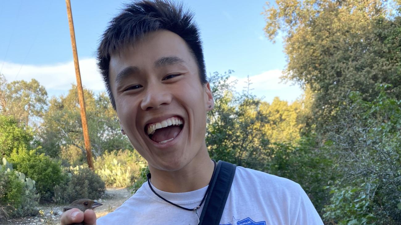 Photo of Cody Pham with big smile, holding a bird for a animal ecology class observation