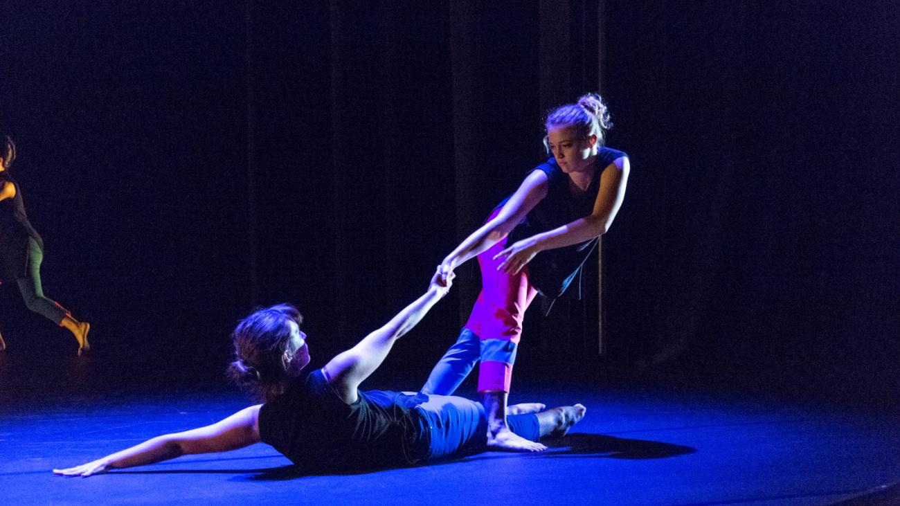 dancer on ground being pulled up by leaning dancer in blue light