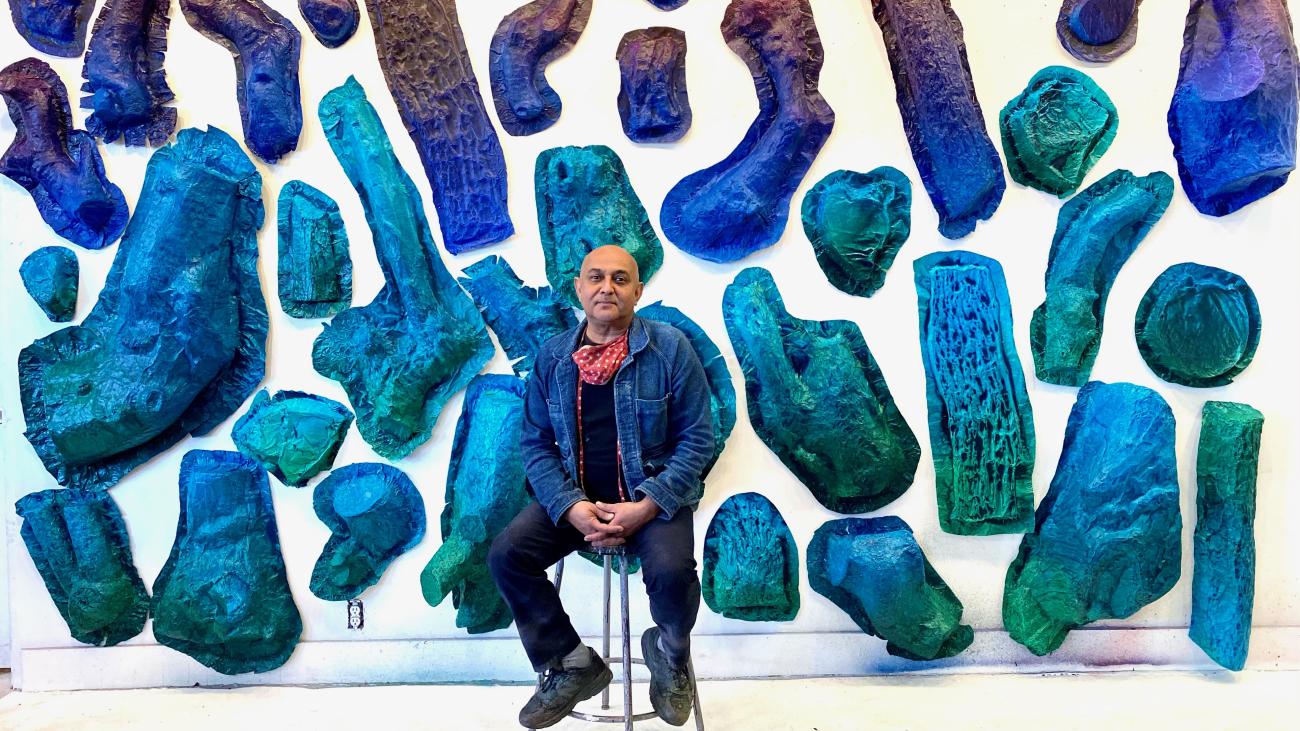 Artist Sandeep Mukherjee seated in front of blue-hued components of his YouTube Theater installation.