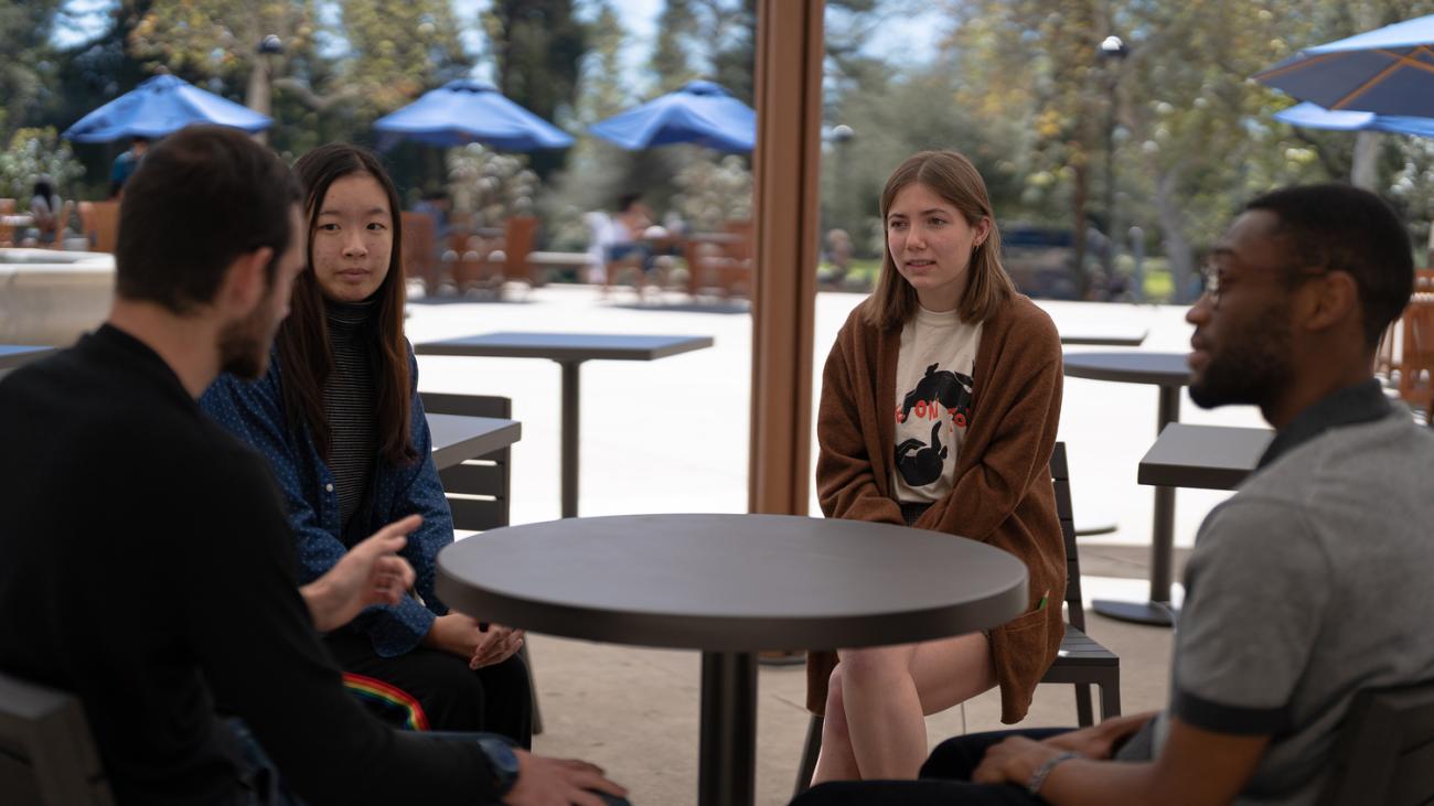 four speaking partners sitting at a table together, talking