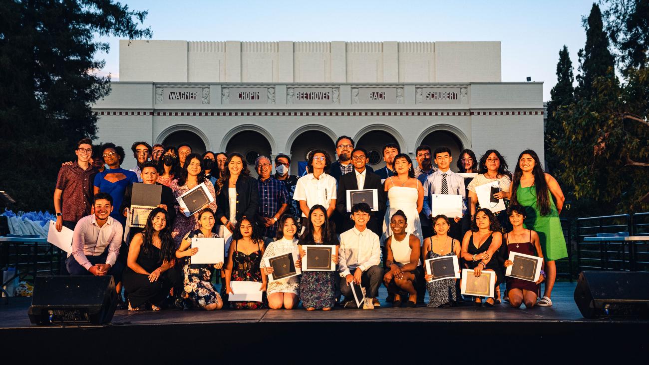 Rising seniors who completed the PAYS program stand in front of Bridges Auditorium holding certificates.