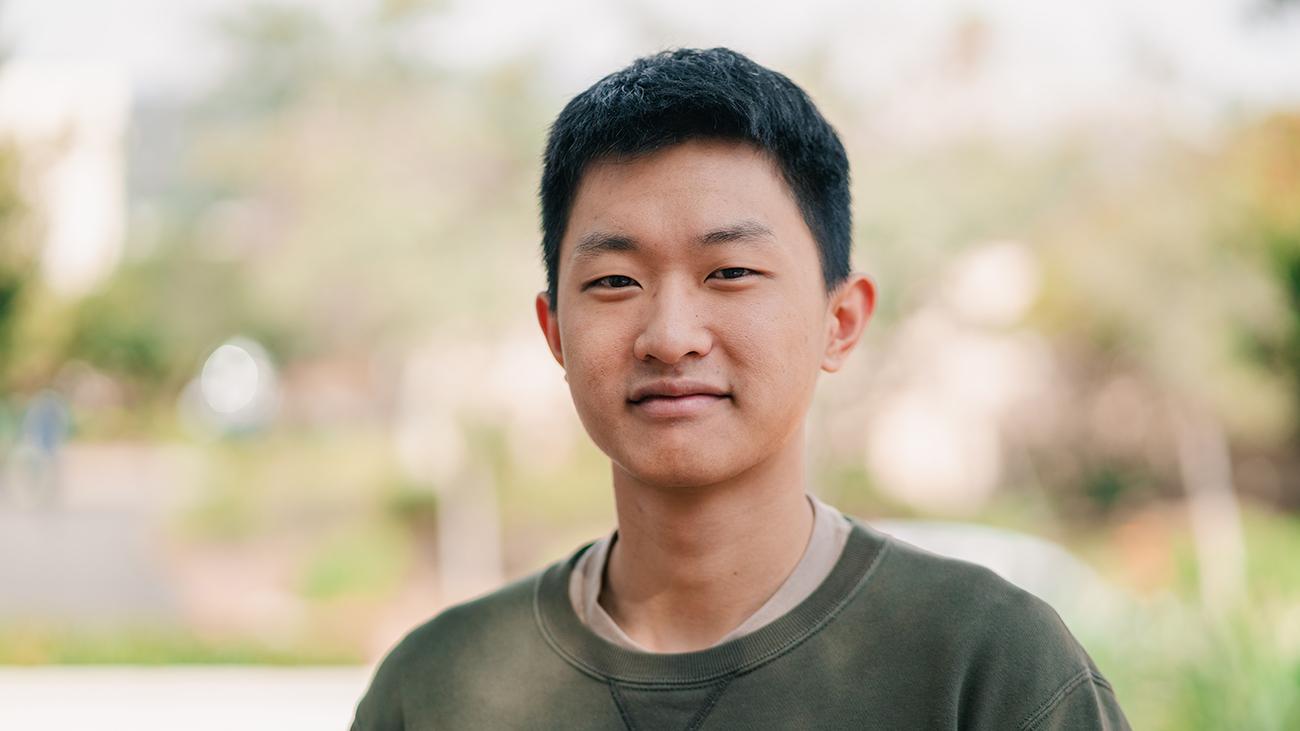 Young man in olive green sweater smiling into camera